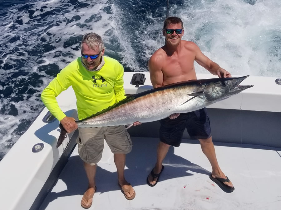 two men holding up a large fish while boating in the ocean