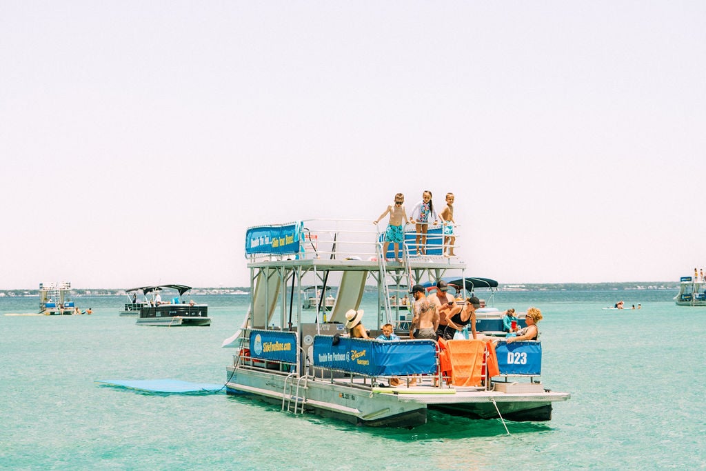 family playing on double decker pontoon boat with two slides in water in destin florida