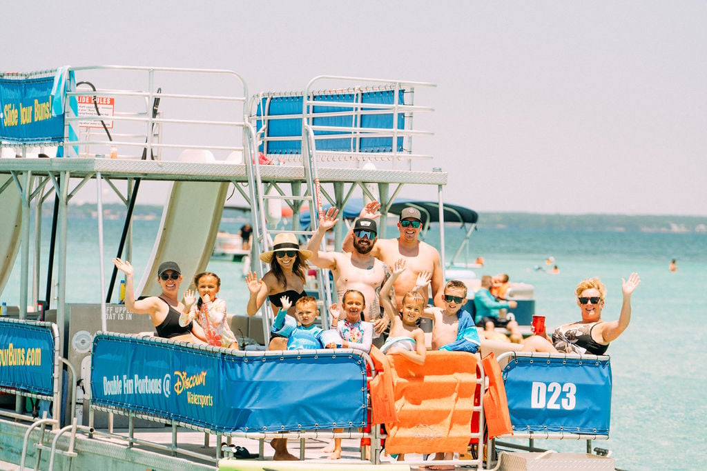 family waving double decker pontoon boat with two slides in water in destin florida