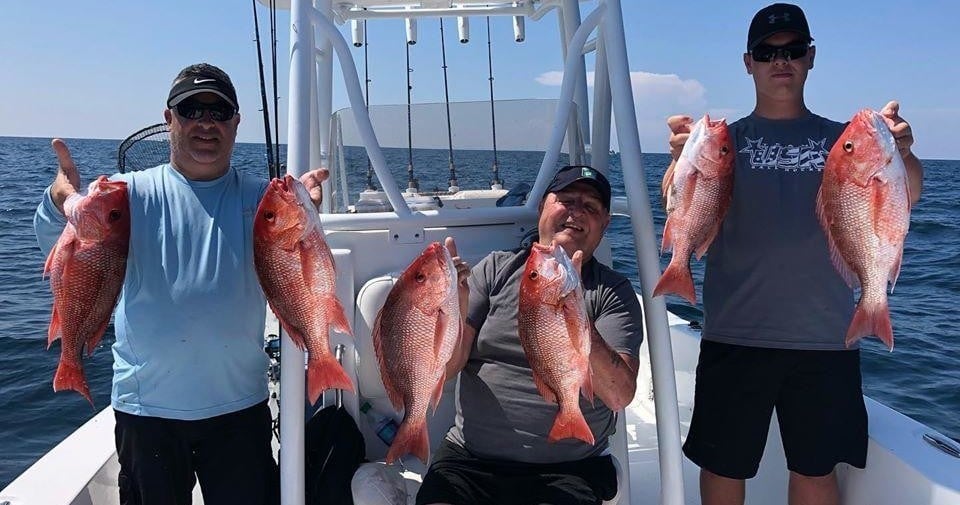 three men holding up red snapper fish that they caught on a fishing charter in destin florida