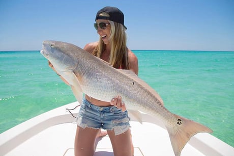 lady with a backwards hat and jean shorts holding a redfish on the front of a sea hunt bay boat