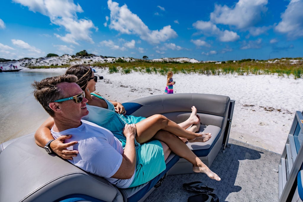 a couple sitting on the front of a pontoon boat pulled up to the beach