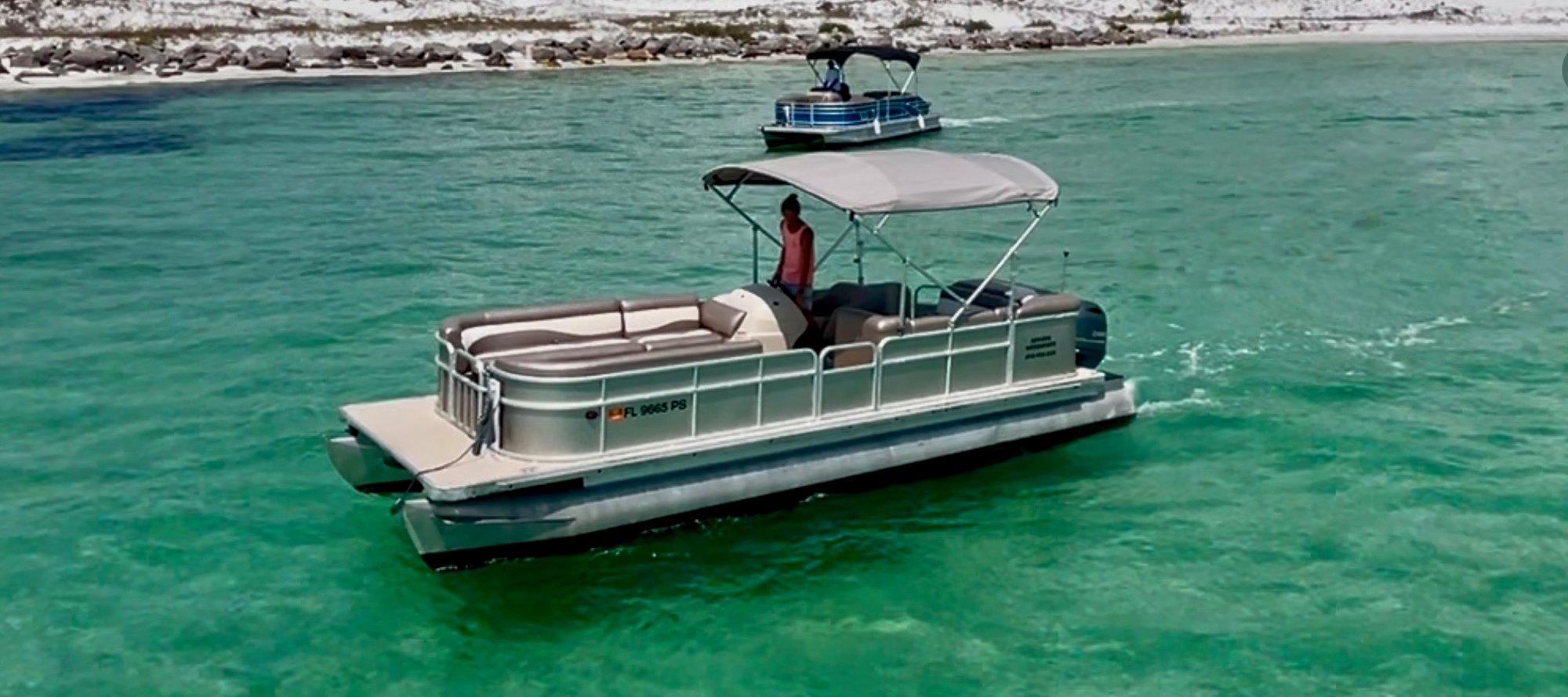 woman driving a pontoon boat through the emerald green waters of destin florida