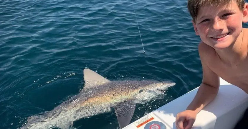 boy next to a shark he just caught off a fishing boat